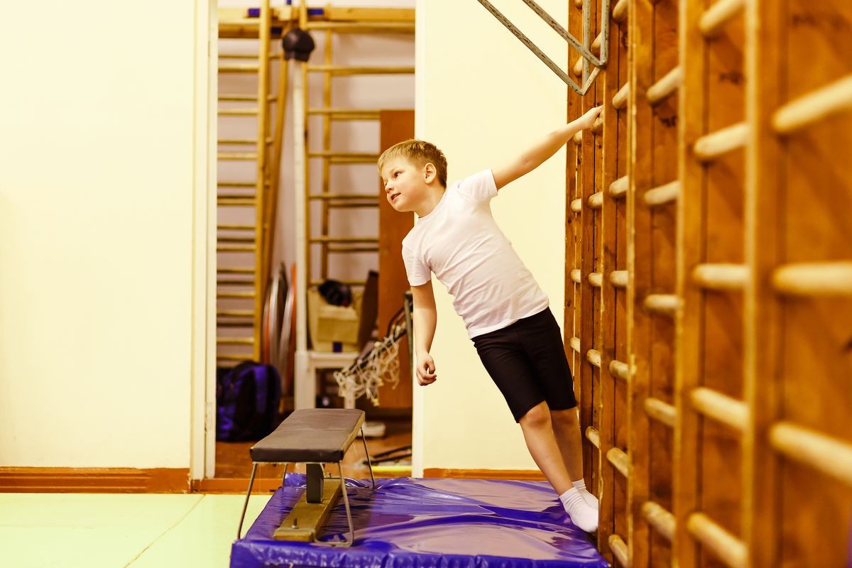 boy hangs on the Swedish wall in the gym