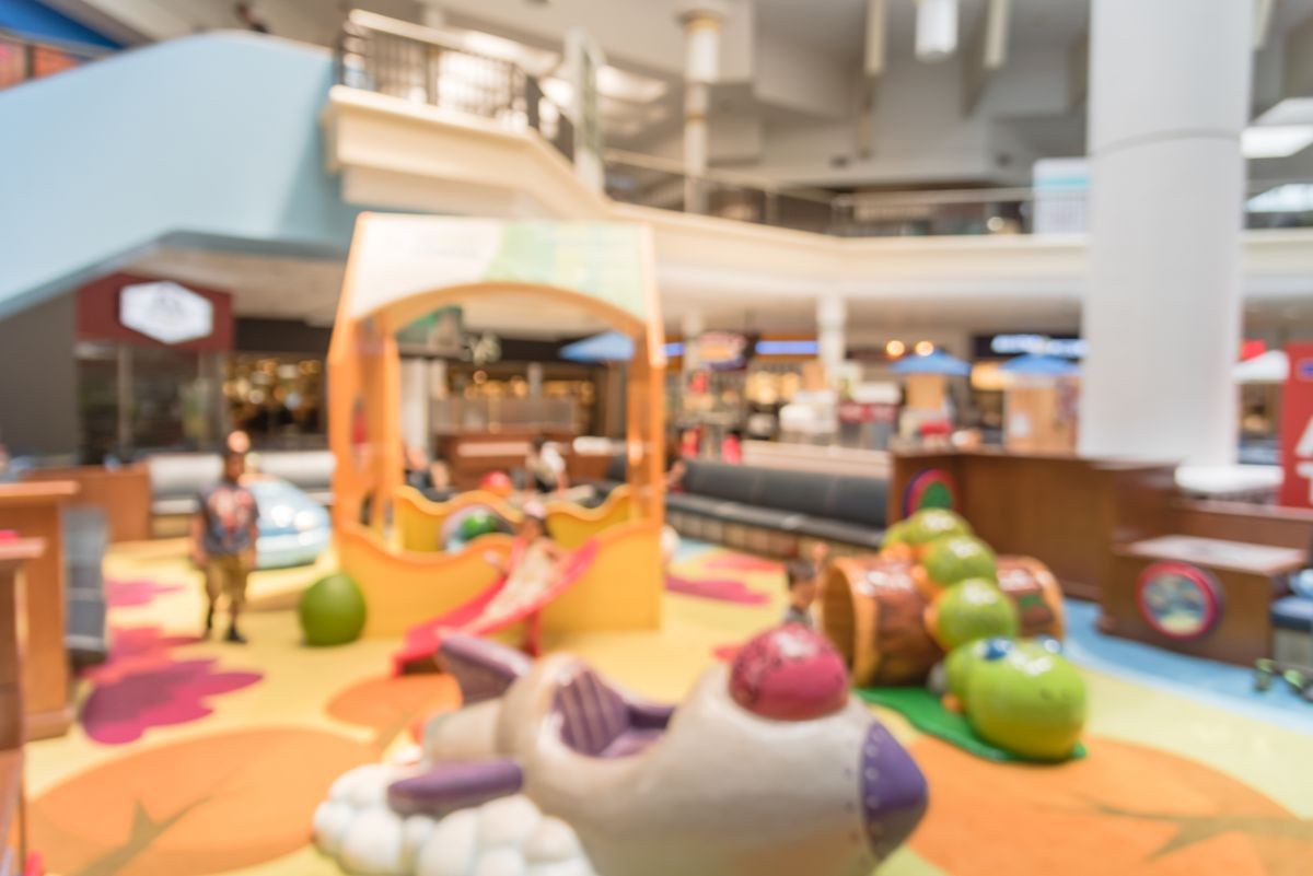 Blurred soft play equipment indoor playground at modern shopping mall in USA. Colorful themed play area with soft climbing structures, slides, tunnels for kids and seating around the edges for parents